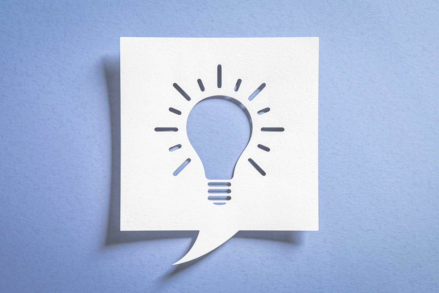 Innovations- und Ideensymbol in Form einer Glühbirne. Weißer Scherenschnitt aus Papier vor blauem Hintergrund.